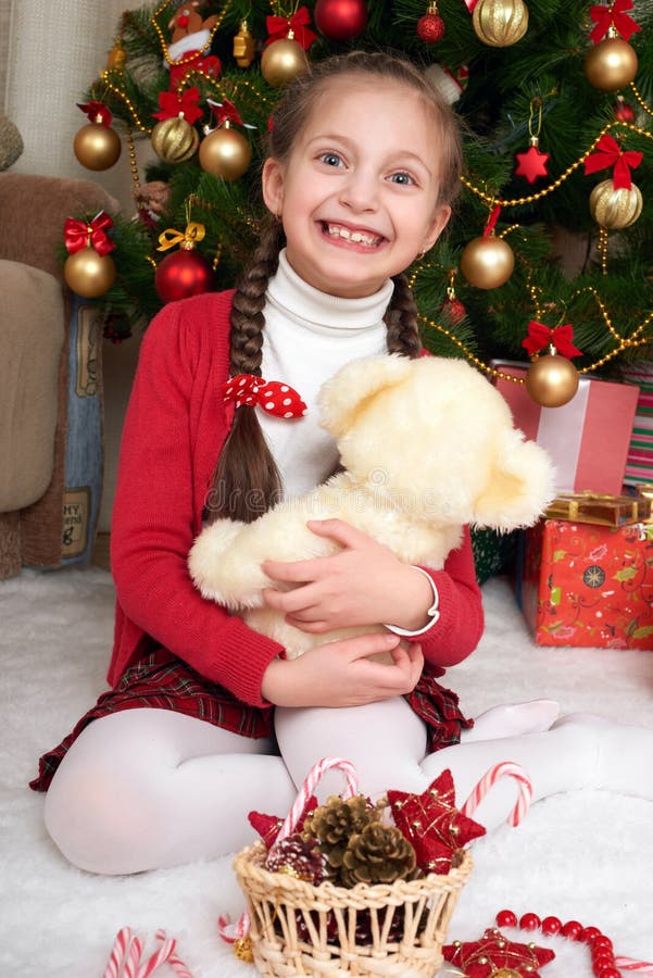 Het meisje zit dichtbij Kerstmis spar en thuis het spelen met beer, Kerstmisdecoratie, gelukkige emotie, het concept van de de wi