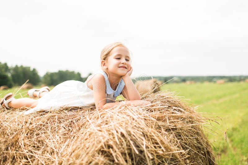 Het meisje zit op een hooiberg, een de zomerconcept royalty-vrije stock afbeelding Het meisje zit op een hooiberg, een de zomerconcept royalty-vrije stock afbeelding