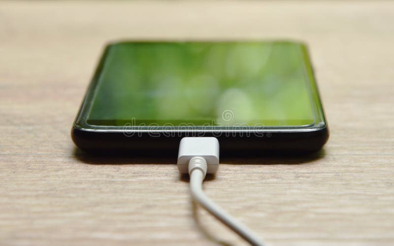 Het mobiele telefoon neersteken in navulbare batterij met witte puinkabel op lijstachtergrond stock afbeeldingen Het mobiele telefoon neersteken in navulbare batterij met witte puinkabel op lijstachtergrond stock afbeeldingen