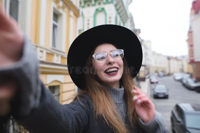 Het modieuze meisje met steunen neemt selfie krasvoho tegen de achtergrond van het stedelijke landschap stock afbeeldingen Het modieuze meisje met steunen neemt selfie krasvoho tegen de achtergrond van het stedelijke landschap stock afbeeldingen