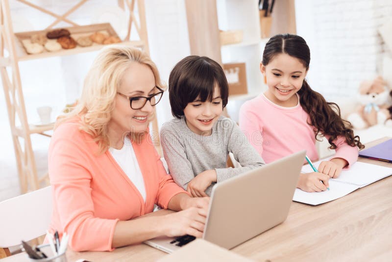 Het mooie bejaarde typen op laptop met haar kleinkinderen stock afbeelding Het mooie bejaarde typen op laptop met haar kleinkinderen stock afbeelding