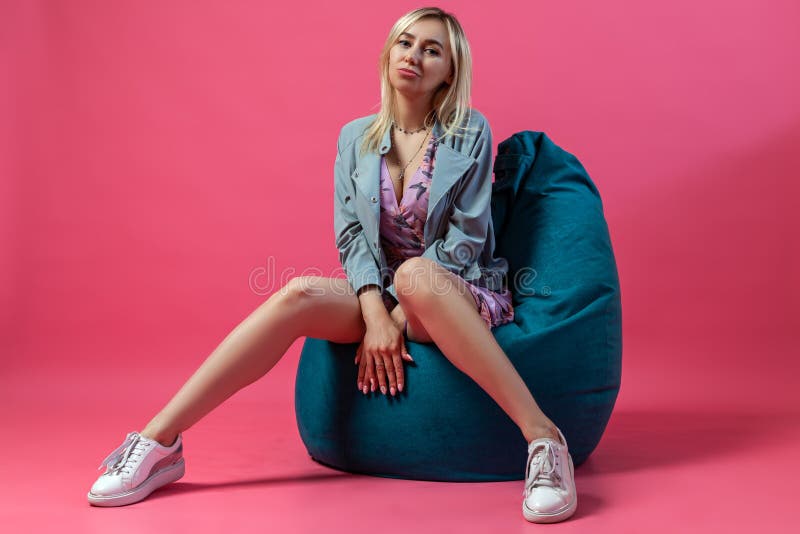Het mooie blondemeisje in een matroos zit apart op een groene zakstoel met haar benen in de vorm van een gevouwen driehoek en han stock fotografie Het mooie blondemeisje in een matroos zit apart op een groene zakstoel met haar benen in de vorm van een gevouwen driehoek en han stock fotografie