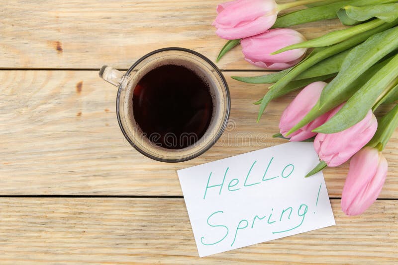 Het mooie boeket van bloemen van roze tulpen, een kop van koffie en de tekst hello springen op papier op een natuurlijke houten a royalty-vrije stock fotografie Het mooie boeket van bloemen van roze tulpen, een kop van koffie en de tekst hello springen op papier op een natuurlijke houten a royalty-vrije stock fotografie