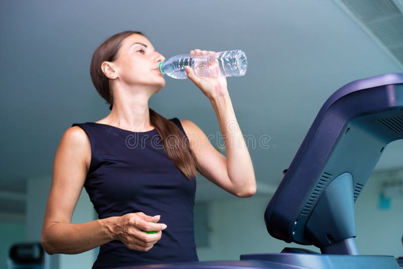 Het mooie geschiktheidsmeisje lopen en drinkwater op tredmolen bij de gymnastiek royalty-vrije stock afbeelding Het mooie geschiktheidsmeisje lopen en drinkwater op tredmolen bij de gymnastiek royalty-vrije stock afbeelding