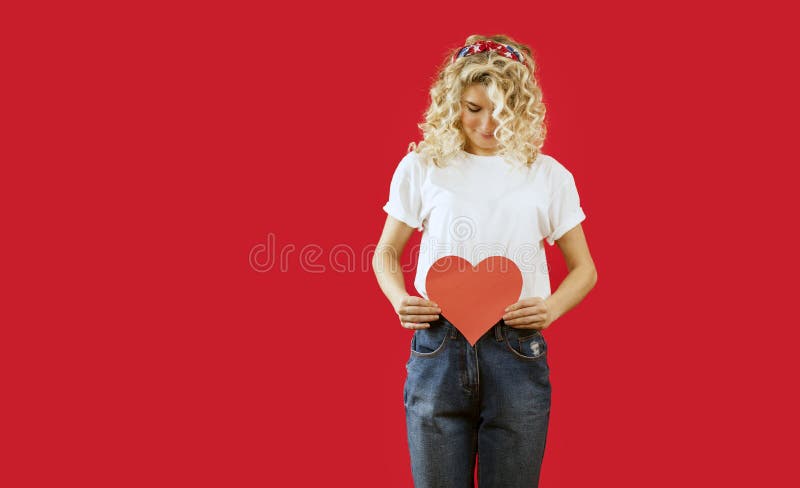 Het mooie jonge emotionele meisje met een rood hart in haar handen bevindt zich op een geïsoleerde rode achtergrond De dag van de stock fotografie Het mooie jonge emotionele meisje met een rood hart in haar handen bevindt zich op een geïsoleerde rode achtergrond De dag van de stock fotografie