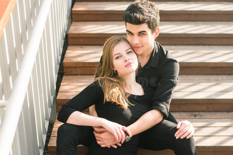 Het mooie jonge multiraciale paar, studentenpaar in liefde, zit houten trap in de stad De mooie Turkse donkerbruine kerel koester stock foto Het mooie jonge multiraciale paar, studentenpaar in liefde, zit houten trap in de stad De mooie Turkse donkerbruine kerel koester stock foto