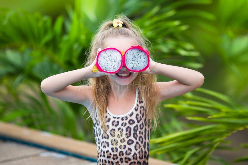 Het mooie kindmeisje spelen met draakfruit dichtbij een zwembad Tropische openluchtachtergrond De ruimte van het exemplaar royalty-vrije stock foto's Het mooie kindmeisje spelen met draakfruit dichtbij een zwembad Tropische openluchtachtergrond De ruimte van het exemplaar royalty-vrije stock foto's
