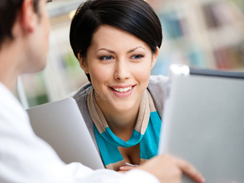 Woman communicates with men showing her something in the tablet sitting at the table at the reading hall. Woman communicates with men showing her something in the tablet sitting at the table at the reading hall