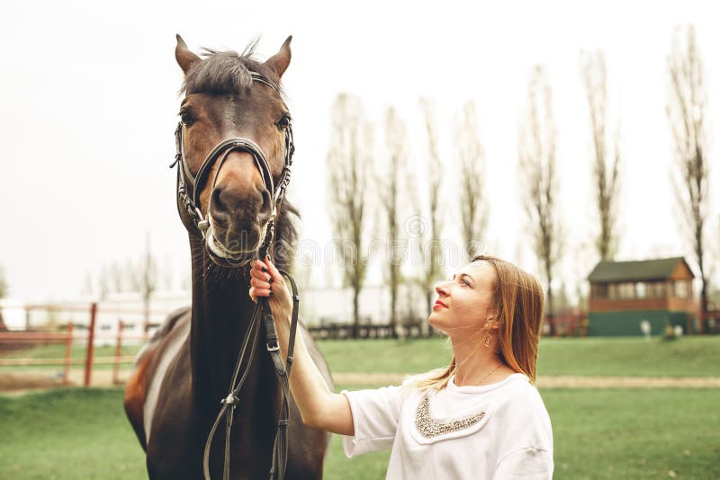 Beautiful girl communicates with the horse in the park. Preparing for the riding. Beautiful girl communicates with the horse in the park. Preparing for the riding