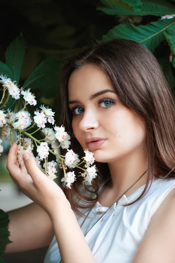 Het mooie meisje die met blond haar en blauwe ogen kastanje houden bloeit in haar hand De lente Lichte make-up en los lang haar royalty-vrije stock foto's Het mooie meisje die met blond haar en blauwe ogen kastanje houden bloeit in haar hand De lente Lichte make-up en los lang haar royalty-vrije stock foto's