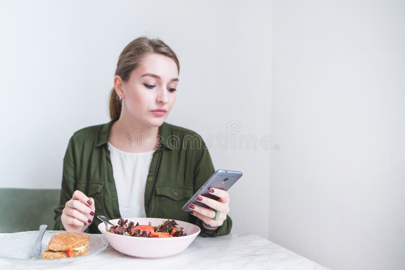 het mooie meisje gebruikt een smearphone terwijl het eten bij het restaurant Een vrouw eet een salade en bekijkt een smartphone stock foto's het mooie meisje gebruikt een smearphone terwijl het eten bij het restaurant Een vrouw eet een salade en bekijkt een smartphone stock foto's