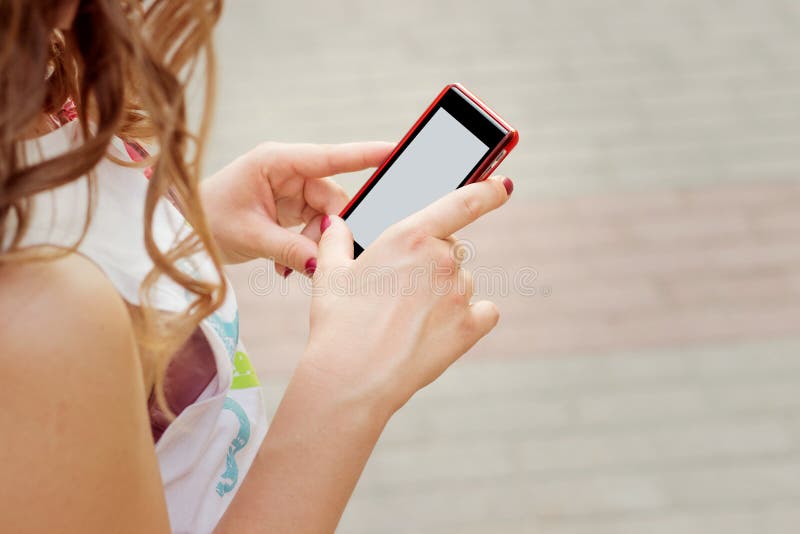 Het mooie meisje met krullend haar die op de straat in telefoon zich ter beschikking bevinden, verzendt een SMS-bericht leest stock foto Het mooie meisje met krullend haar die op de straat in telefoon zich ter beschikking bevinden, verzendt een SMS-bericht leest stock foto