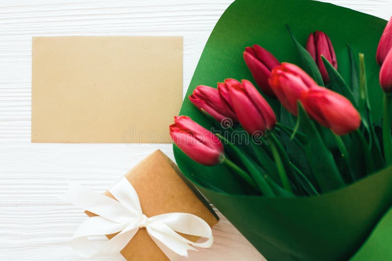 Het mooie rode tulpenboeket in Groenboek, giftvakje en ambachtkaart met ruimte voor tekst op witte houten vlakte als achtergrond stock foto's Het mooie rode tulpenboeket in Groenboek, giftvakje en ambachtkaart met ruimte voor tekst op witte houten vlakte als achtergrond stock foto's
