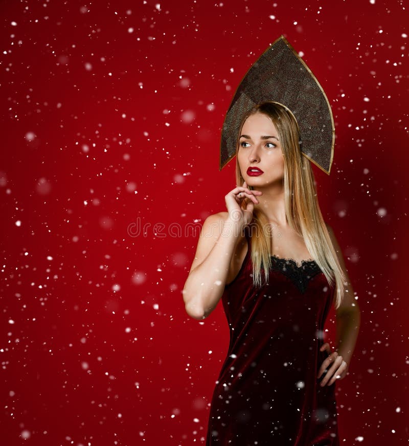 Het mooie sexy blonde Russische meisje in traditionele kokoshnikhoed, fluweel feestelijke kleding op een rode achtergrond, kijkt royalty-vrije stock foto Het mooie sexy blonde Russische meisje in traditionele kokoshnikhoed, fluweel feestelijke kleding op een rode achtergrond, kijkt royalty-vrije stock foto