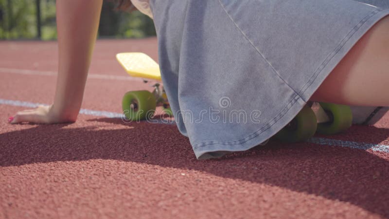 Het niet erkende tienermeisje zit op een skateboard bij openluchtbasketbalhof zonnig zomerweer in de. Sport concept