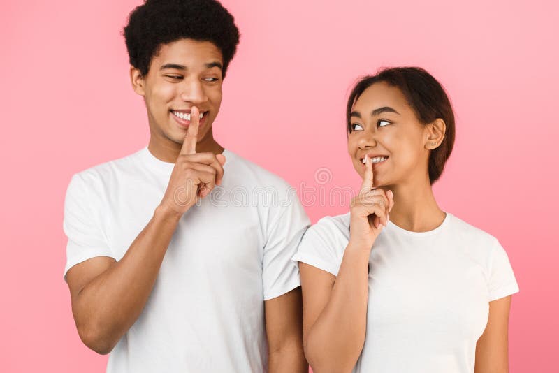 It`s our secret. Teens holding fingers on lips and looking at each other, pink studio background. It`s our secret. Teens holding fingers on lips and looking at each other, pink studio background