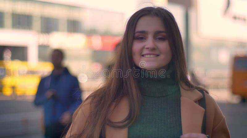 Het ontzagwekkende Kaukasische wijfje bevindt zich een zijweg en bekijkt recht met gelukkig gezicht die camera, op stadsgebied on