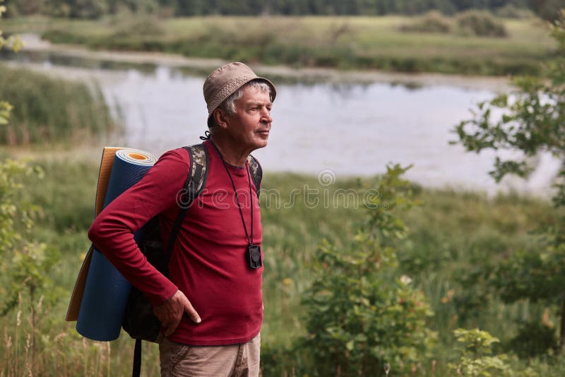 Het openluchtschot van de elderymens met rugzak en deken, het hogere mannelijke poing in openlucht met handen op heupen, beslist stock afbeeldingen Het openluchtschot van de elderymens met rugzak en deken, het hogere mannelijke poing in openlucht met handen op heupen, beslist stock afbeeldingen