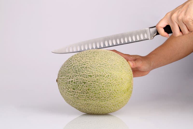 Het organische fruit van de Kantaloepmeloen met in hand isolat van het keukenmes stock afbeelding Het organische fruit van de Kantaloepmeloen met in hand isolat van het keukenmes stock afbeelding