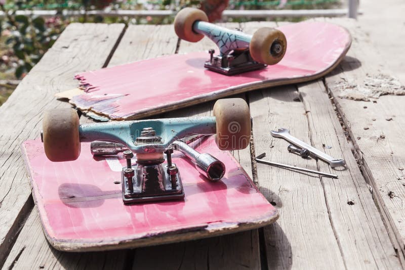 Het oude gebroken skateboard ligt met een moersleutel op een houten lijst in openlucht stock afbeelding Het oude gebroken skateboard ligt met een moersleutel op een houten lijst in openlucht stock afbeelding