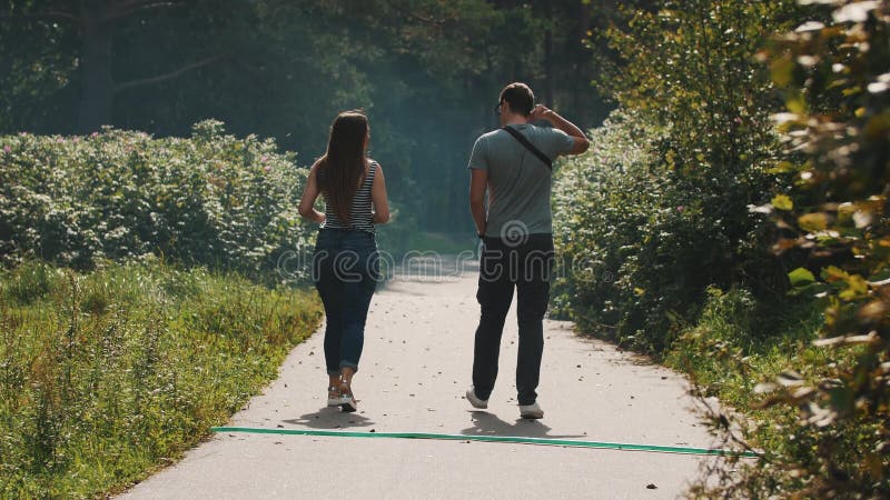 Het paar loopt vanaf camera langs een asfaltweg in een park op een winderige dag