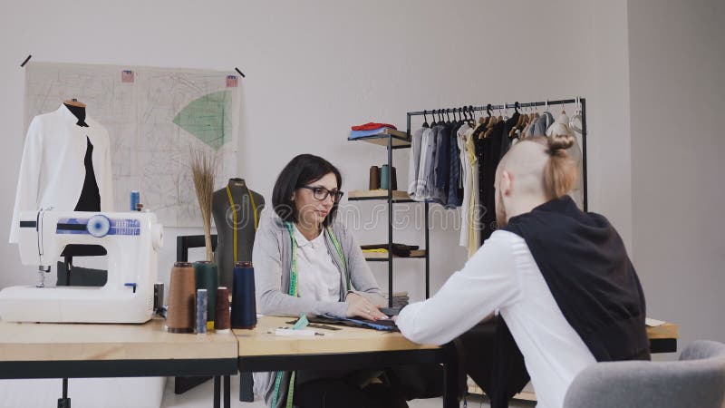 Het paar van manierontwerpers werkt in workshop De aantrekkelijke jonge vrouw in glazen en de modieuze gebaarde man zijn binnen