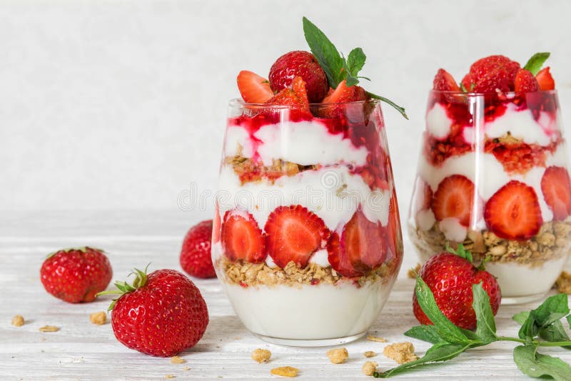 Het parfait van de aardbeiyoghurt met granola, munt en verse bessen in glazen op witte houten lijst Gezond Ontbijt