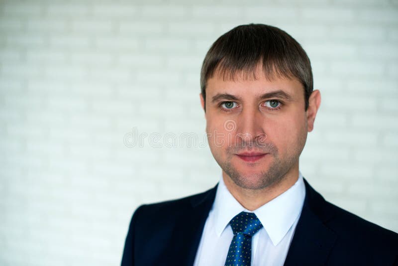 Het portret die van het close-upgezicht van een mens in een pak en een band, zich voor een witte bakstenen muurachtergrond bevind stock afbeelding Het portret die van het close-upgezicht van een mens in een pak en een band, zich voor een witte bakstenen muurachtergrond bevind stock afbeelding