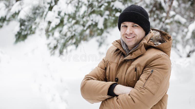 Het portret van een knappe jonge mens in een rood jasje in een de winterbos de man kruiste zijn wapens over zijn borst royalty-vrije stock afbeelding Het portret van een knappe jonge mens in een rood jasje in een de winterbos de man kruiste zijn wapens over zijn borst royalty-vrije stock afbeelding