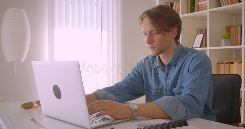 Het portret van een succesvolle kaukasische zakenman die een laptop gebruikt die camera's binnen in kantoor bekijkt