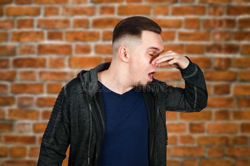 Het portret van Kaukasische kerel, dichte neus, stinkt Mens op bakstenen muurachtergrond stock fotografie Het portret van Kaukasische kerel, dichte neus, stinkt Mens op bakstenen muurachtergrond stock fotografie