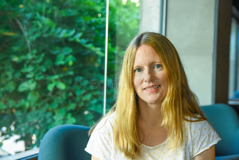 Het portret van mooie jonge Kaukasische vrouw met blauwe ogen van het leng de blonde haar zit in Europese Amerikaanse koffiezitka stock afbeelding Het portret van mooie jonge Kaukasische vrouw met blauwe ogen van het leng de blonde haar zit in Europese Amerikaanse koffiezitka stock afbeelding