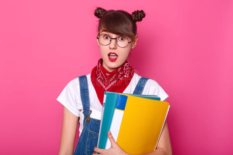 Het portret van student met twee bossen, draagt witte t-shirt, denimoverall, rode bandana en rond gemaakte glazen, houdend colouu stock afbeelding Het portret van student met twee bossen, draagt witte t-shirt, denimoverall, rode bandana en rond gemaakte glazen, houdend colouu stock afbeelding