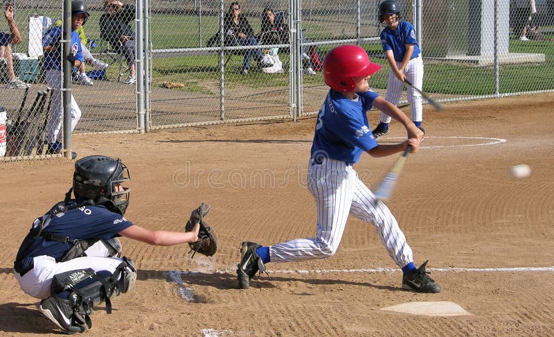 A pony baseball game as a hitter is about to make impact with a ball. A catcher reaches out for the ball. A pony baseball game as a hitter is about to make impact with a ball. A catcher reaches out for the ball.