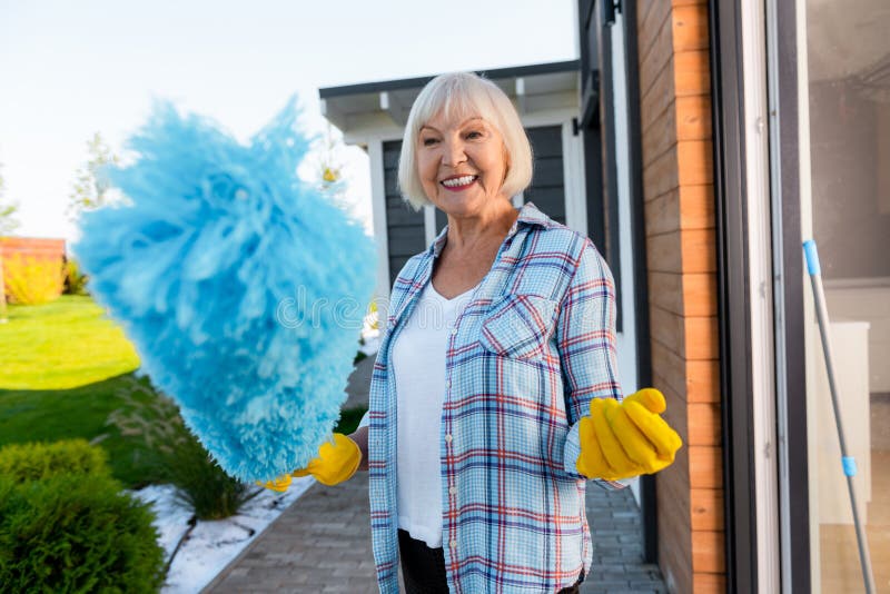Het richten van blonde-haired bejaarde dame die het schoonmaken doen dichtbij de zomerhuis stock foto Het richten van blonde-haired bejaarde dame die het schoonmaken doen dichtbij de zomerhuis stock foto