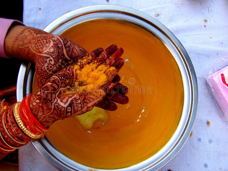 A groom and his bride wash their mehendi applied hands in the same bowl with haldi(turmeric powder) as a part of a ritual in Indian Marriages. A groom and his bride wash their mehendi applied hands in the same bowl with haldi(turmeric powder) as a part of a ritual in Indian Marriages.