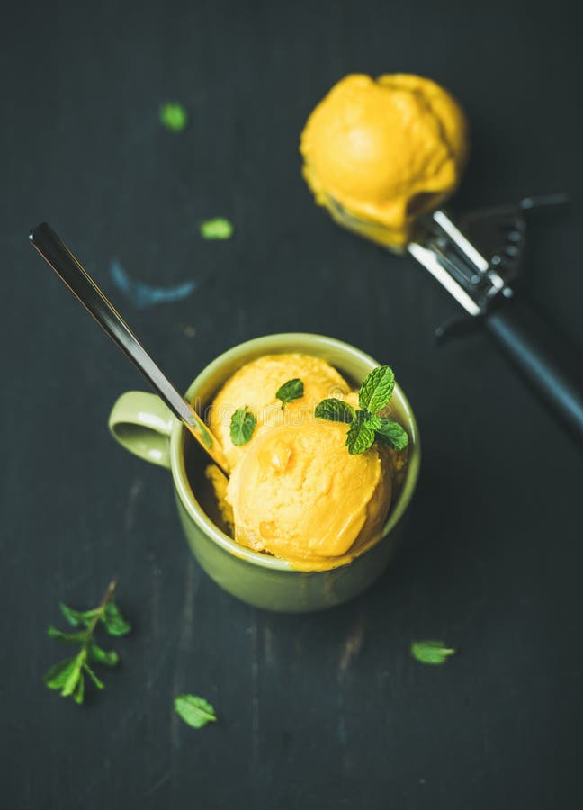 Het roomijslepels van de mangosorbet met munt, zwarte houten achtergrond stock foto's Het roomijslepels van de mangosorbet met munt, zwarte houten achtergrond stock foto's