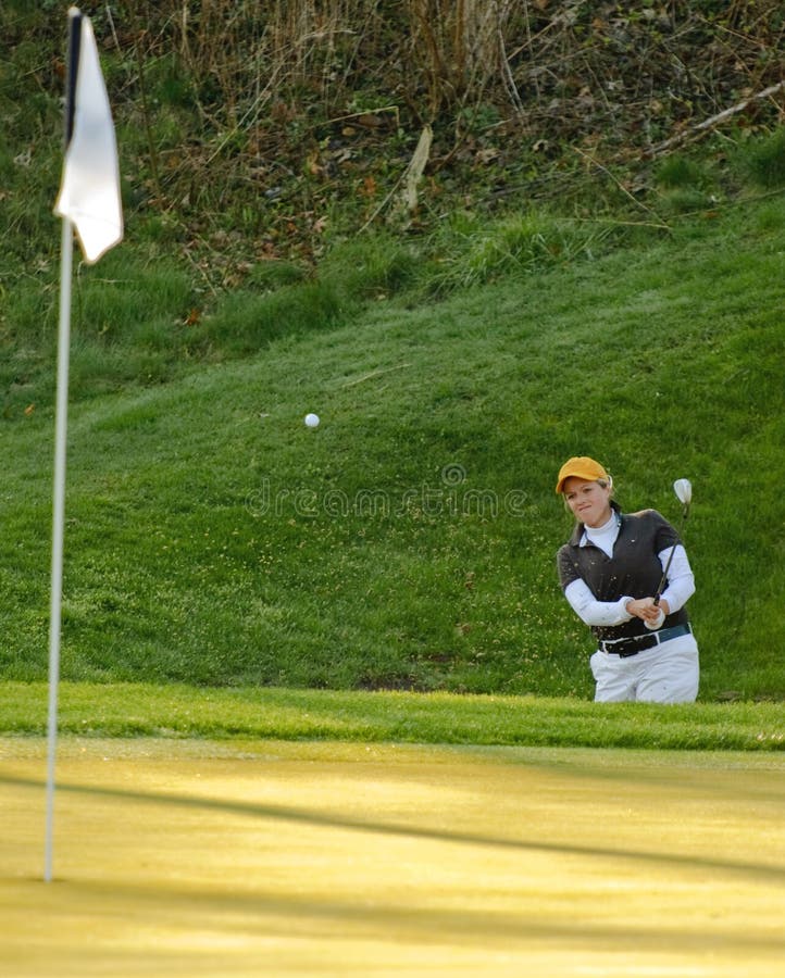 Collegiate woman golfer hitting the ball out of the sand trap. Collegiate woman golfer hitting the ball out of the sand trap