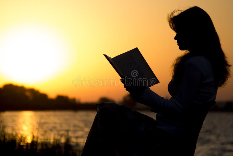 Het silhouet van een jonge mooie vrouw bij dageraadzitting op het vouwen zit en zorgvuldig het staren bij het open boek voor stock afbeelding Het silhouet van een jonge mooie vrouw bij dageraadzitting op het vouwen zit en zorgvuldig het staren bij het open boek voor stock afbeelding