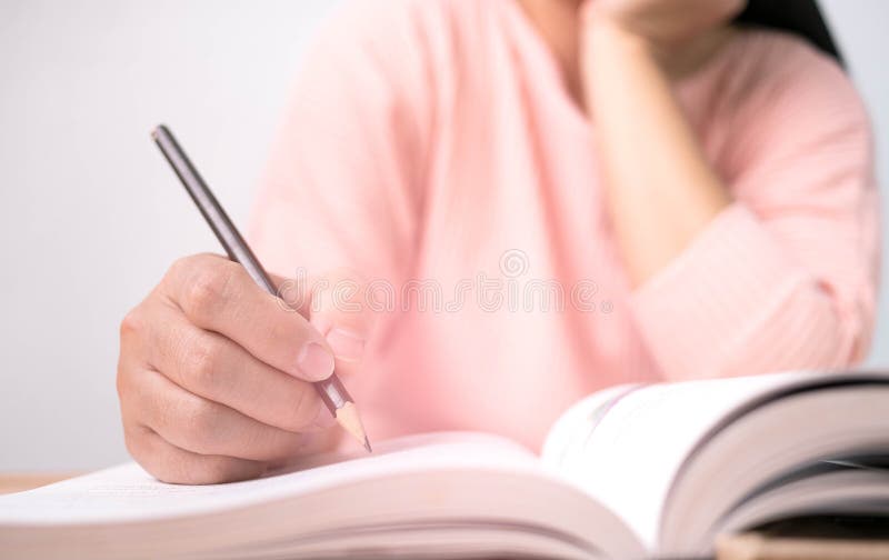 Close up of Woman`s hand drawing a line and writing short summary while reading a book at library. Close up of Woman`s hand drawing a line and writing short summary while reading a book at library.