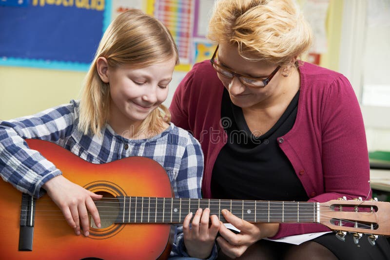Het Spelgitaar van leraarshelping pupil to in Muziekles stock afbeelding Het Spelgitaar van leraarshelping pupil to in Muziekles stock afbeelding