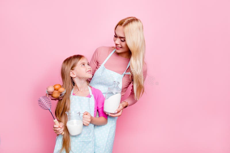 Het studioportret van moeder en dochter, die noodzakelijke ingrediënten voor cake hebben, die aan elkaar kijken, klaar voor kok, stock fotografie Het studioportret van moeder en dochter, die noodzakelijke ingrediënten voor cake hebben, die aan elkaar kijken, klaar voor kok, stock fotografie