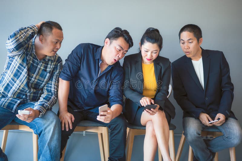 Het team van bedrijfs Aziatische mensen is opgewekt over de informatie over smartphone van de groepsleden terwijl het wachten op royalty-vrije stock afbeeldingen Het team van bedrijfs Aziatische mensen is opgewekt over de informatie over smartphone van de groepsleden terwijl het wachten op royalty-vrije stock afbeeldingen
