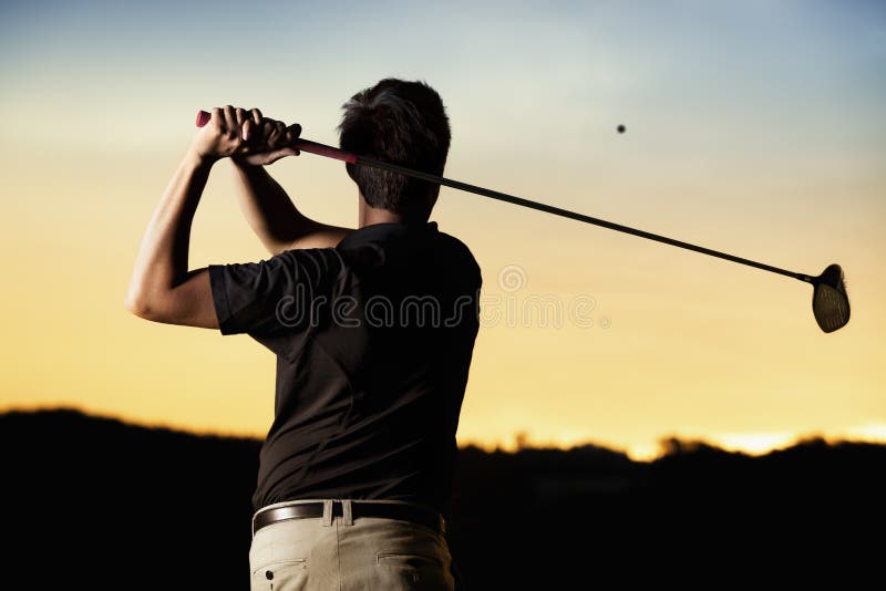 Close up professional golf player in black shirt teeing-off ball in twilight, view from behind. Close up professional golf player in black shirt teeing-off ball in twilight, view from behind.