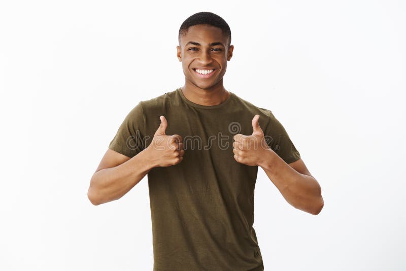 Friendly handsome masculine african american joyful man showing thumbs up gesture and smiling broadly, liking idea or product giving positive feedback, expressing good opinion, cheering over grey wall. Friendly handsome masculine african american joyful man showing thumbs up gesture and smiling broadly, liking idea or product giving positive feedback, expressing good opinion, cheering over grey wall.