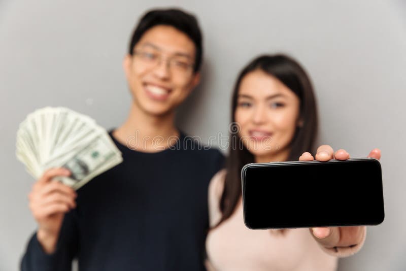 Het vrolijke jonge Aziatische het houden van geld van de paarholding en het tonen van vertoning van mobiele telefoon stock foto Het vrolijke jonge Aziatische het houden van geld van de paarholding en het tonen van vertoning van mobiele telefoon stock foto
