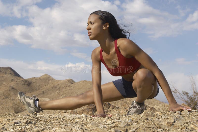 Mixed race female jogger stretching in mountains against cloudy sky. Mixed race female jogger stretching in mountains against cloudy sky