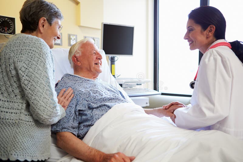 Female Doctor Talking To Senior Couple In Hospital Room Looking At Patient Smiling. Female Doctor Talking To Senior Couple In Hospital Room Looking At Patient Smiling