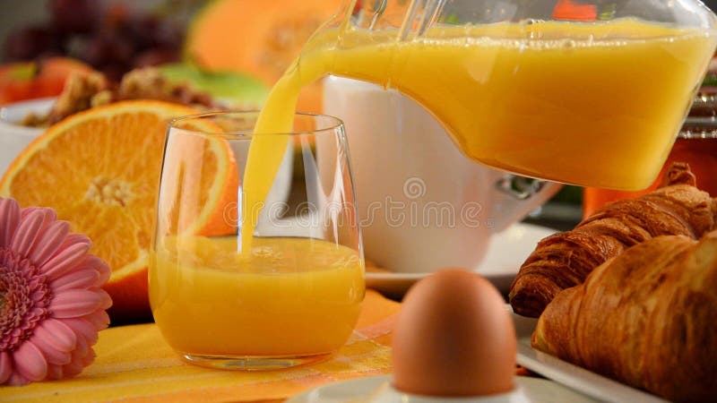 Het vullen van glas met jus d'orange op lijst met ontbijt