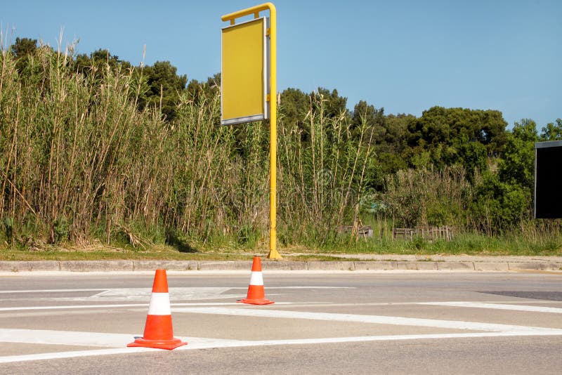 Het werk aangaande weg Bouwkegels met gele advertentieraad bij straat Verkeerskegels, met witte en oranje strepen op asfalt stock afbeelding Het werk aangaande weg Bouwkegels met gele advertentieraad bij straat Verkeerskegels, met witte en oranje strepen op asfalt stock afbeelding